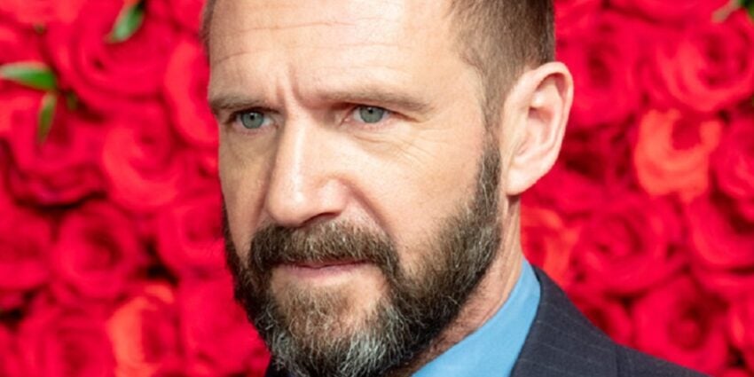 Actor Ralph Fiennes seen close-up in front of a wall of red roses