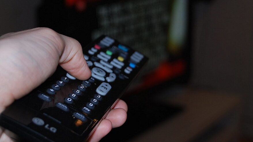 A hand seen holding a TV remote control