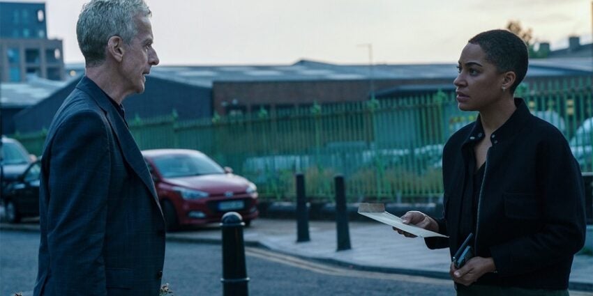 Peter Capaldi and Cush Jumbo stand facing each other on a quiet road