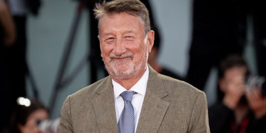 Peaky Blinders creator Steven Knight standing up in a beige tweed jacket and grey tie