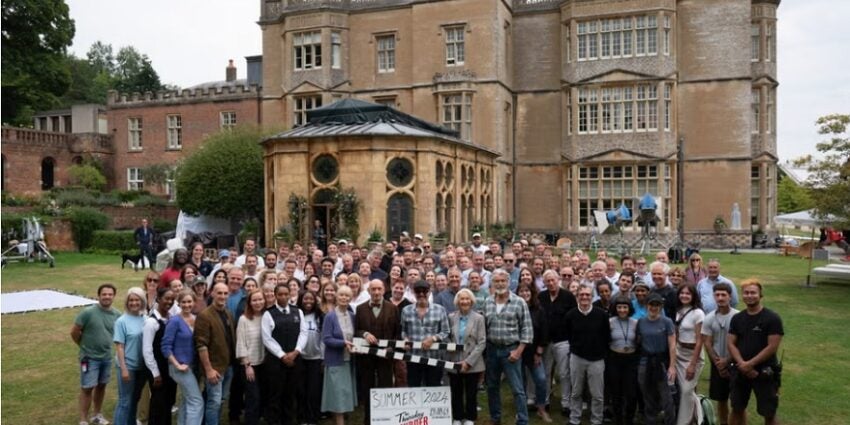 Large group of cast and crew of The Thursday Murder Club standing in front of an old building