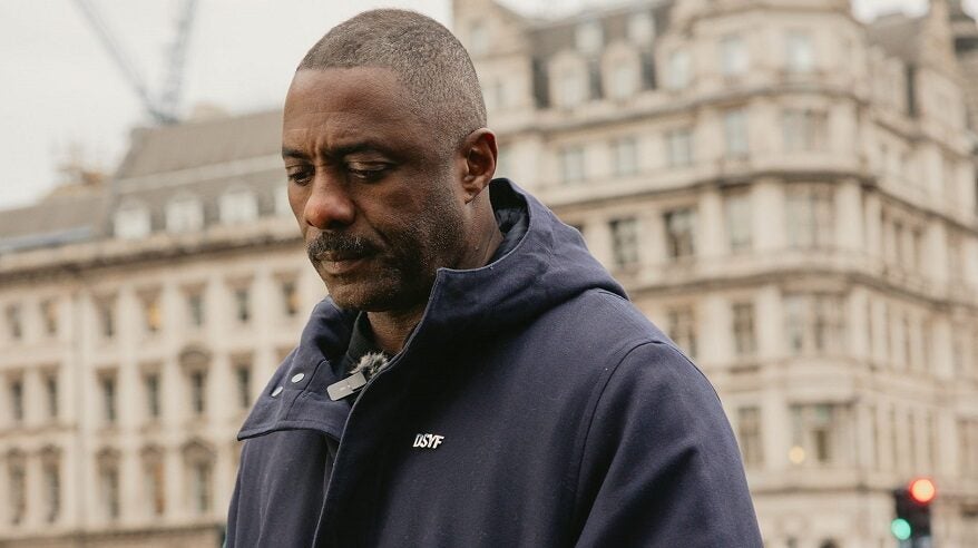 Actor Idris Elbalooking downwards in a street