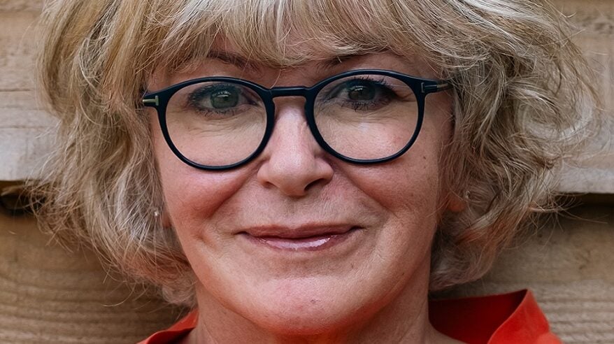 Lisa Opie seen close-up with fluffy blonde hair, round glasses and an orange collar