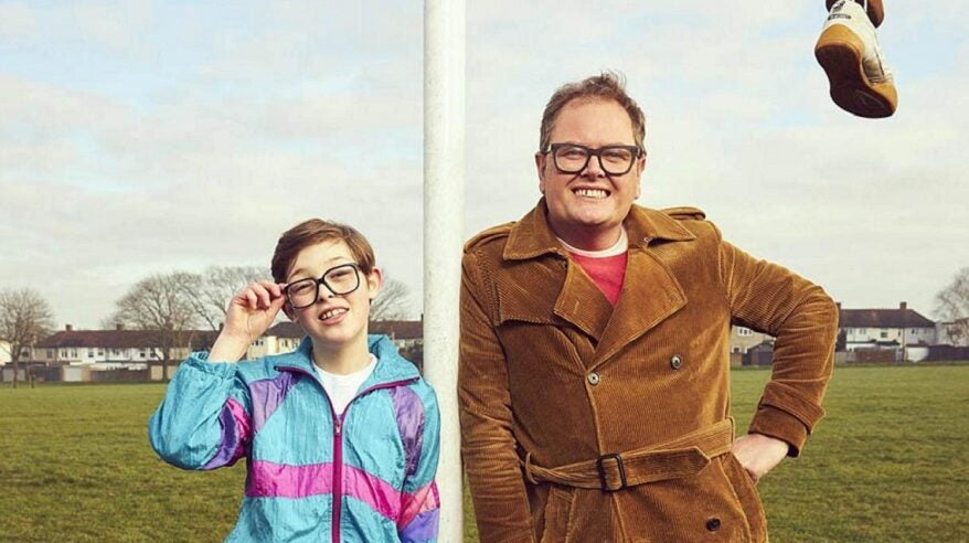 Alan Carr and a young actor stand on a field in front of a football goalpost in ITV's comedy Changing Ends