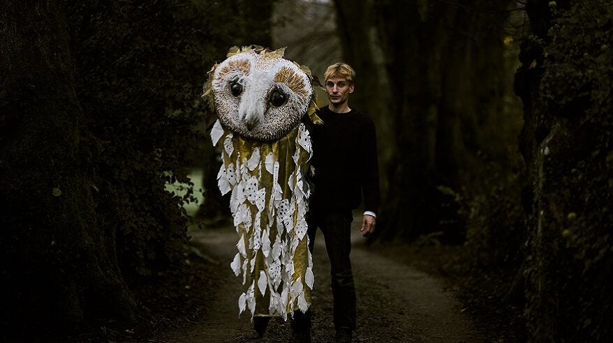 Charlie Cooper stands in dark forest with large owl costume