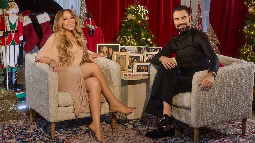 Singing superstar Mariah Carey sitting opposite presenter Rylan with Christmas decorations and a Christmas tree in the background