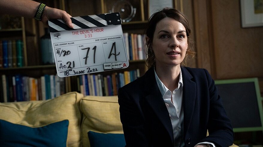 Actor Jessica Raine sitting on a sofa behind a clapperboard for drama The Devil's Hour