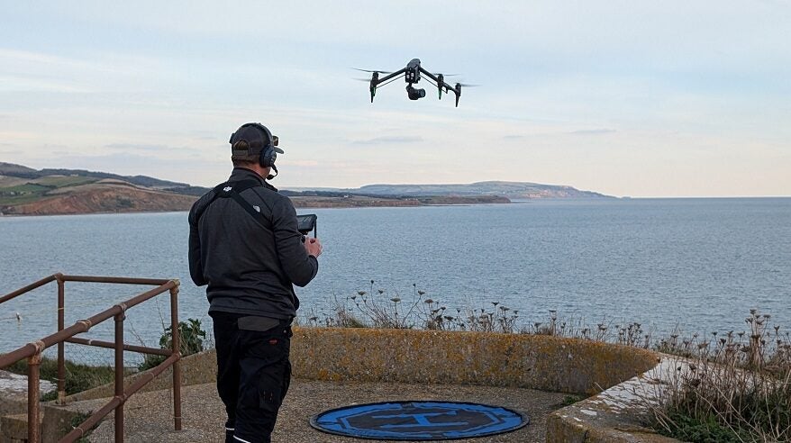 Drone flying over the sea on Isle of Wight with operator in the foreground