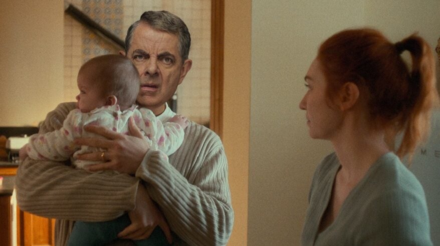 Actor Rowan Atkinson pulling a face while holding a baby in Netflix comedy Man vs Baby