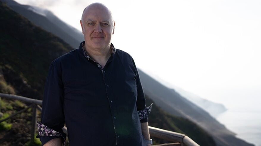 Dara Ó Briain standing in front of a volcano