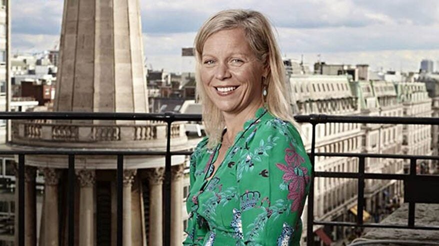 Charlotte Moor of the BBC wearing green printed dress and standing against backdrop of London rooftops