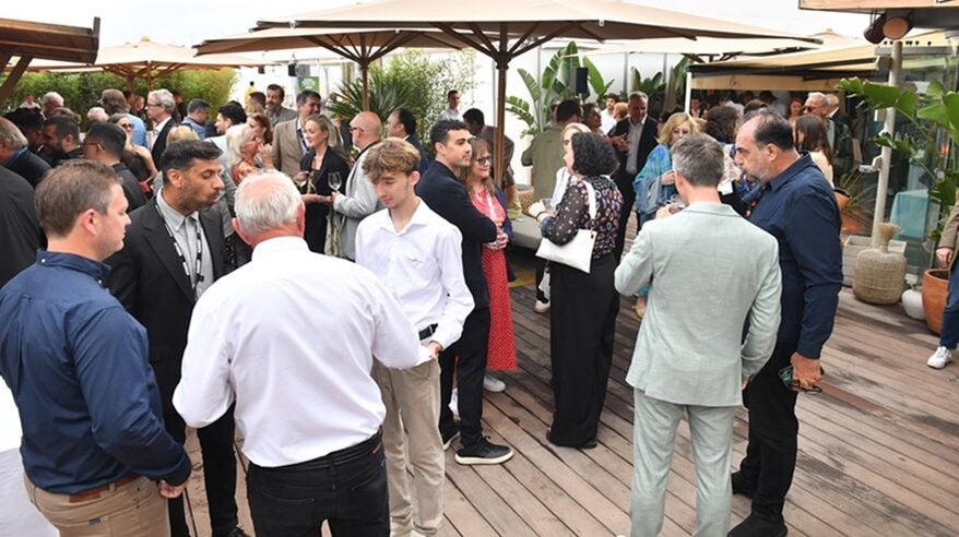 Group of people socialising outdoors on wooden decking with parasols and plants