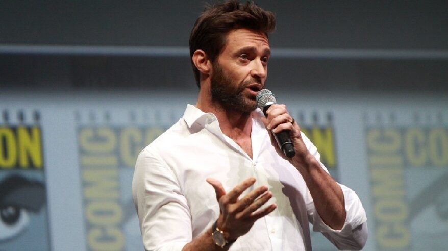 Actor Hugh Jackman wearing white shirt and speaking while holding a microphone