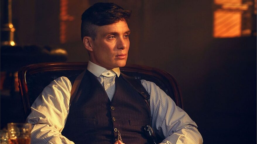 Actor Cillian Murphy in character as Tommy Shelby in Peaky Blinders, seated and wearing a 1920s style white shirt with dark waistcoat