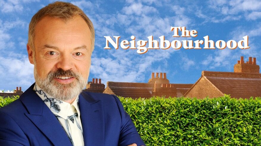 TV host Graham Norton standing in front of a promotional picture for the ITV show The Neighbourhood