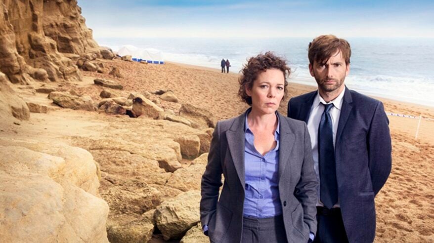 Olivia Colman and David Tennant in TV drama Broadchurch, standing on a beach with cliffs and sea behind