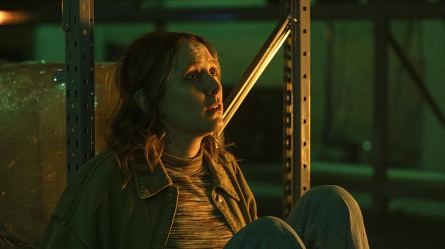 Actor Rose Ayling-Ellis in ITV drama Code of Silence, sitting crouched on the floor against metal shelving