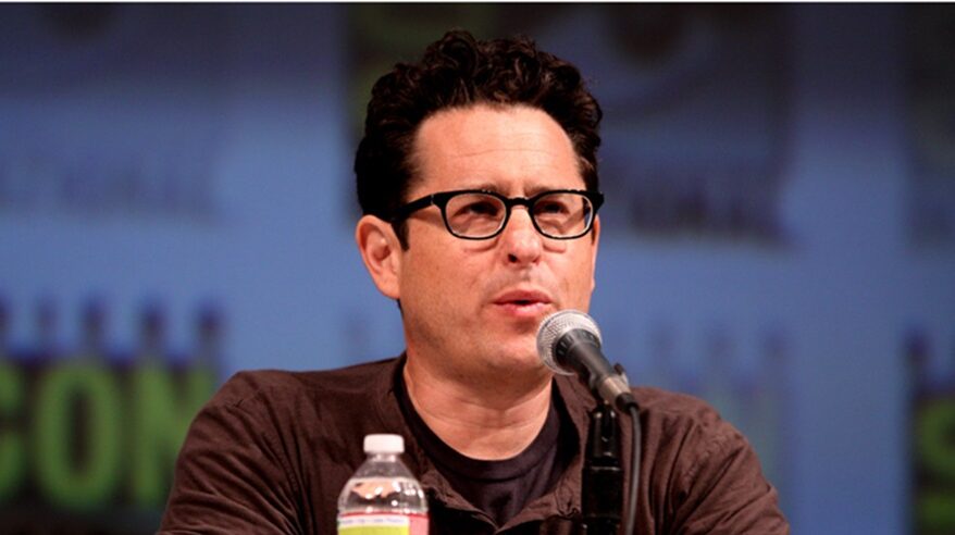 Director JJ Abrams in brown T-shirt and glasses, seated with a microphone and water bottle in front of him