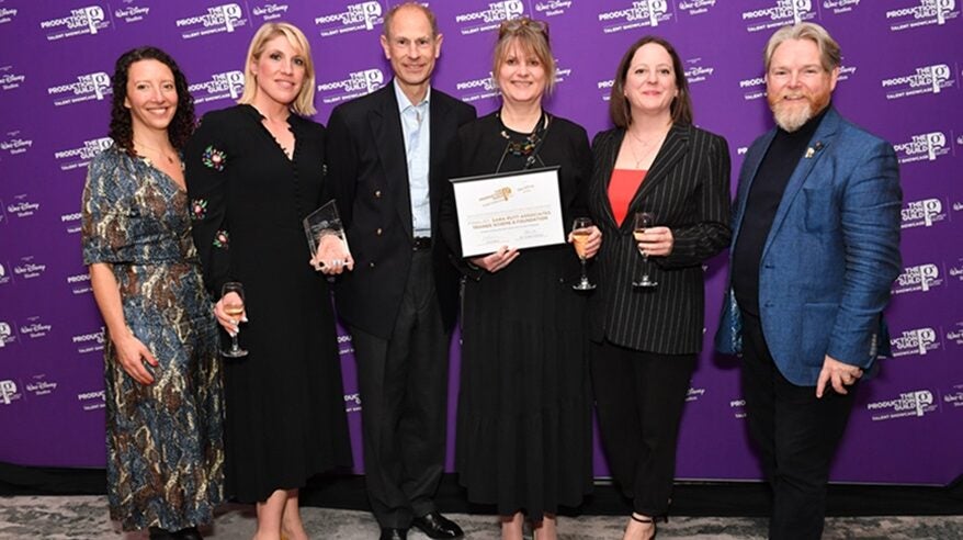 Group of women standing in a row in front of a purple logo-ed background, with HRH the Duke of Edinburgh in the middle