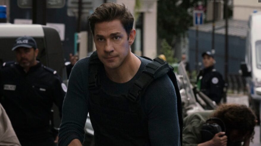 Actor John Krasinski in character as Jack Ryan wearing a dark top and a backpack