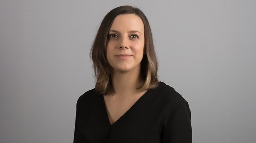 Headshot of Lisa Firetto, wearing dark v-necked top against grey background