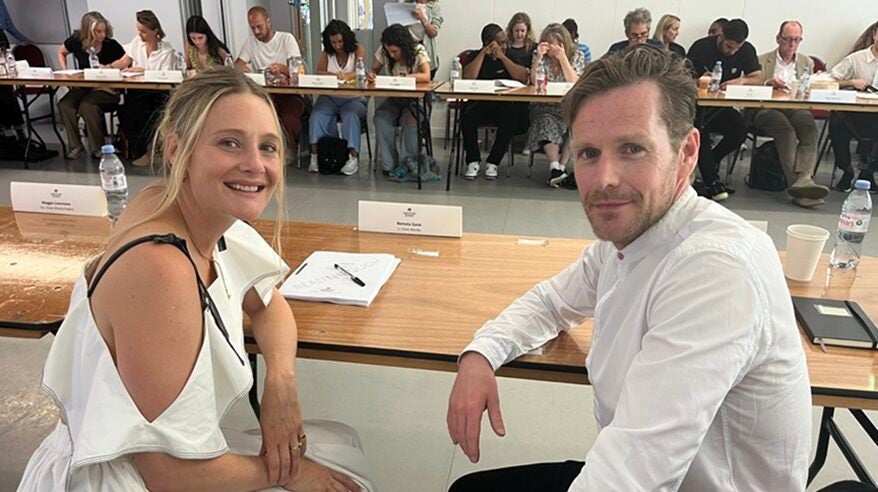 Actors Romola Garai and Shaun Evans at a large table, turning to face the camera, both wearing white