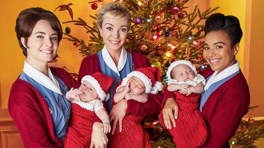 Photo from BBC period drama Call the Midwife, with three nurses holding babies in front of a Christmas tree