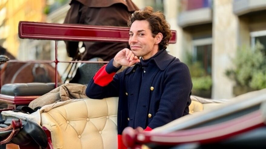 Presenter Tom Read Wilson in navy military jacket sitting in a horse-drawn carriage with chin on hand