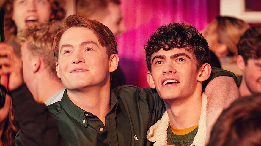 Two young actors in Heartstopper against a pink curtain background