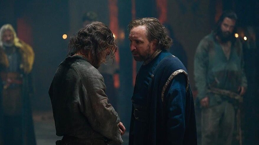 Two actors wearing medieval costume stand face to face in a dark setting, from ITV drama The Winter King