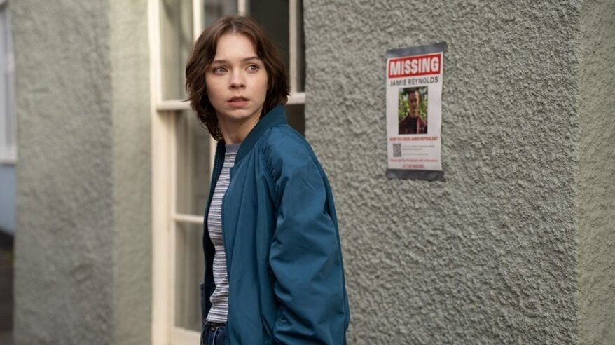 Young girl standing in front of a grey wall with a missing person's poster on it