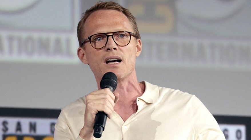 Actor Paul Bettany in pale sweater with glasses, holding a microphone