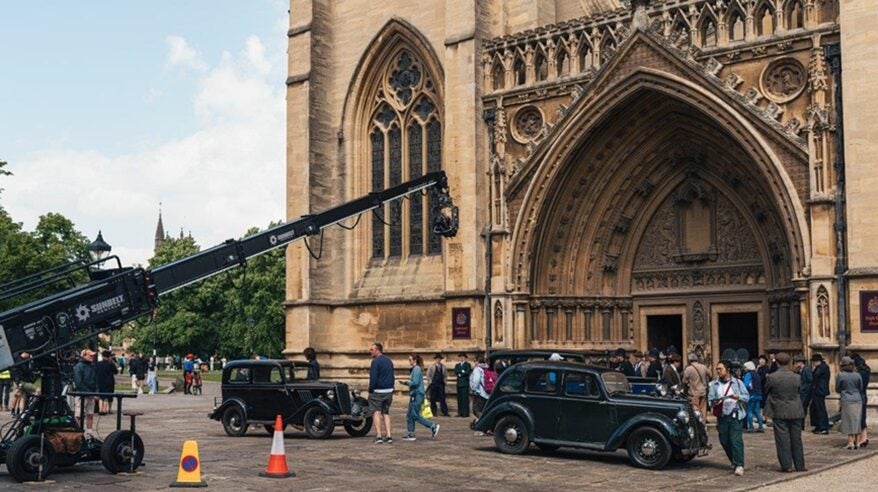 Film crew outside a cathedral with period cars