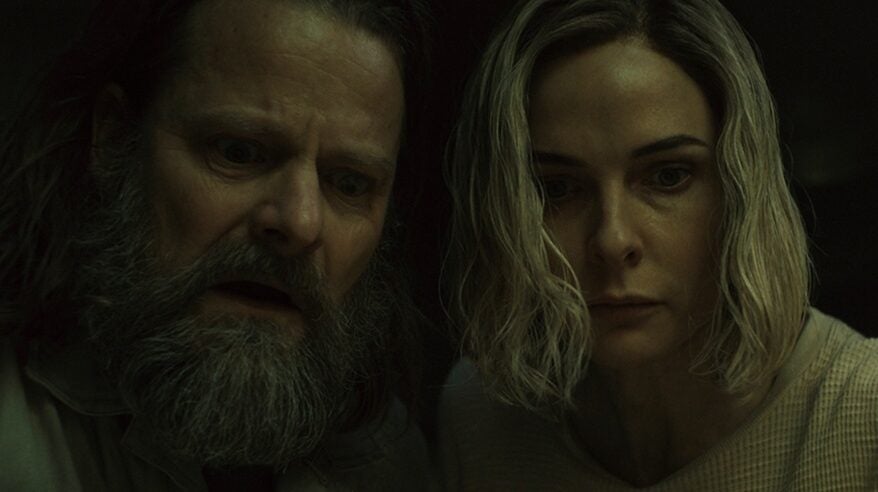 Dark image of a bearded man and a lady with blonde hair looking out towards the camera from Apple TV+ drama Silo