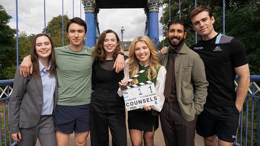 Cast of BBC drama Counsels stand on a bridge with one of the women holding a clapperboard