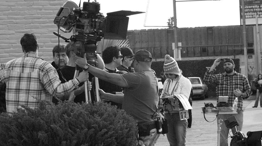 Black and white photo of film crew outside with hedge in foreground
