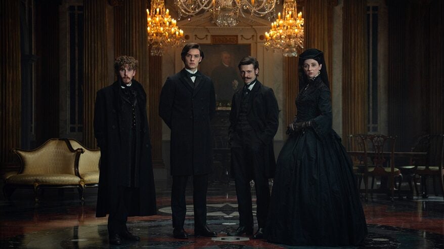 Four people in elegant, dark19th century costume stand in a grand room with huge chandeliers overhead, in a scene from Netflix drama House of Guinness
