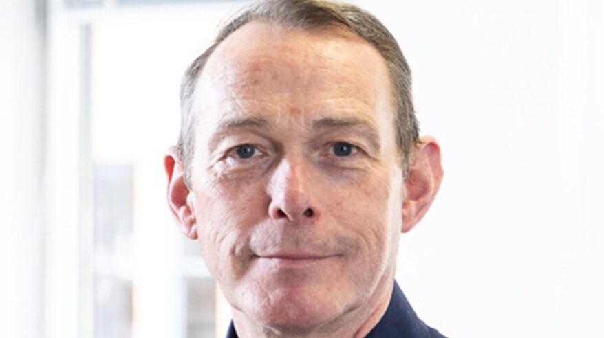 Close-up of a man with short brown hair looking straight at camera, with dark blue collar visible
