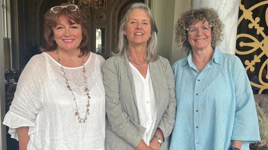 Three ladies stand together in pastel clothes against smart interior background