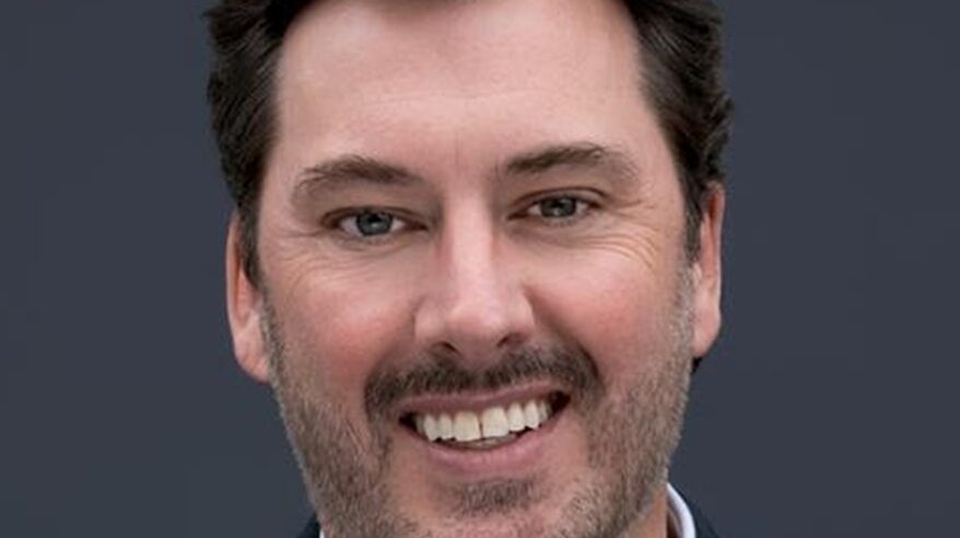 Close-up pic of a man smiling at the camera, with light moustache and beard and dark hair