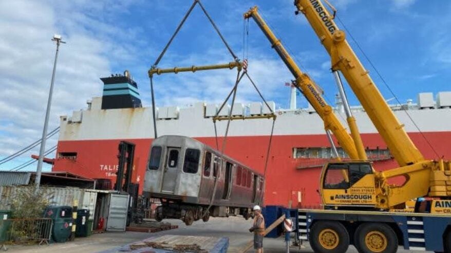 A large yellow crane lifts a old train carriage up.